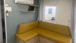 Ein Zimmer mit gelber Couch, Fenster mit Blick, Klimaanlage und Tür.