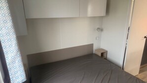 Ein Schlafzimmer mit einem Bett, einem Kopfteil, einem kleinen Nachttisch und einem Fenster mit Vorhängen.