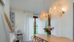 Un coin repas avec une table en bois, des suspensions en osier et un vase rempli de fleurs.