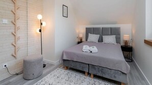 Une chambre moderne avec un lit gris, un mur en briques blanches, une lampe sur pied et une table de chevet avec une lampe.