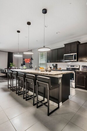 A modern kitchen with a central island, bar stools, dark cabinets, and stainless steel appliances. - NEW! Star Wars Galactic Landing - Minutes to Disney World! Pool, Hot tub, Themed (Kissimmee)
