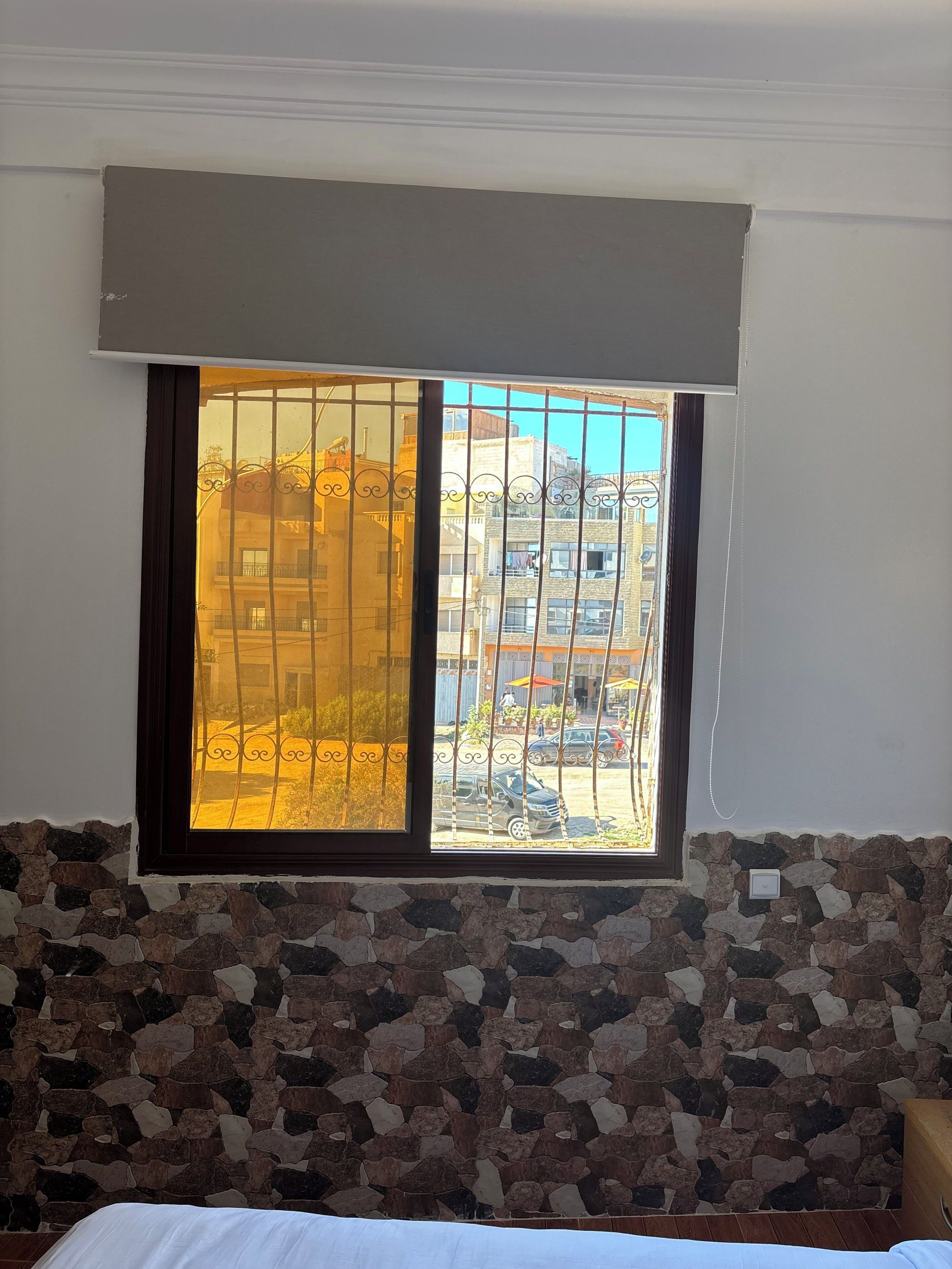 Una habitación con pared de piedra, una ventana con rejas y una cama.