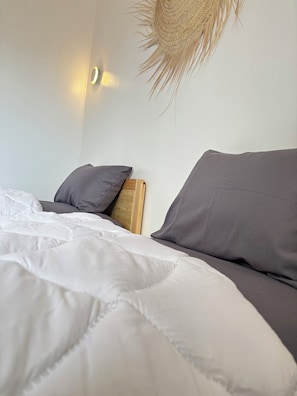 A neatly made bed with white and grey bedding, a woven wall hanging, and a wall-mounted light fixture. - Tifawave surf stay tamraght (Tamraght)