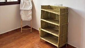 A room with a wooden floor, a window with a view of buildings, and a bamboo shelf unit. - Tifawave surf stay tamraght (Tamraght)