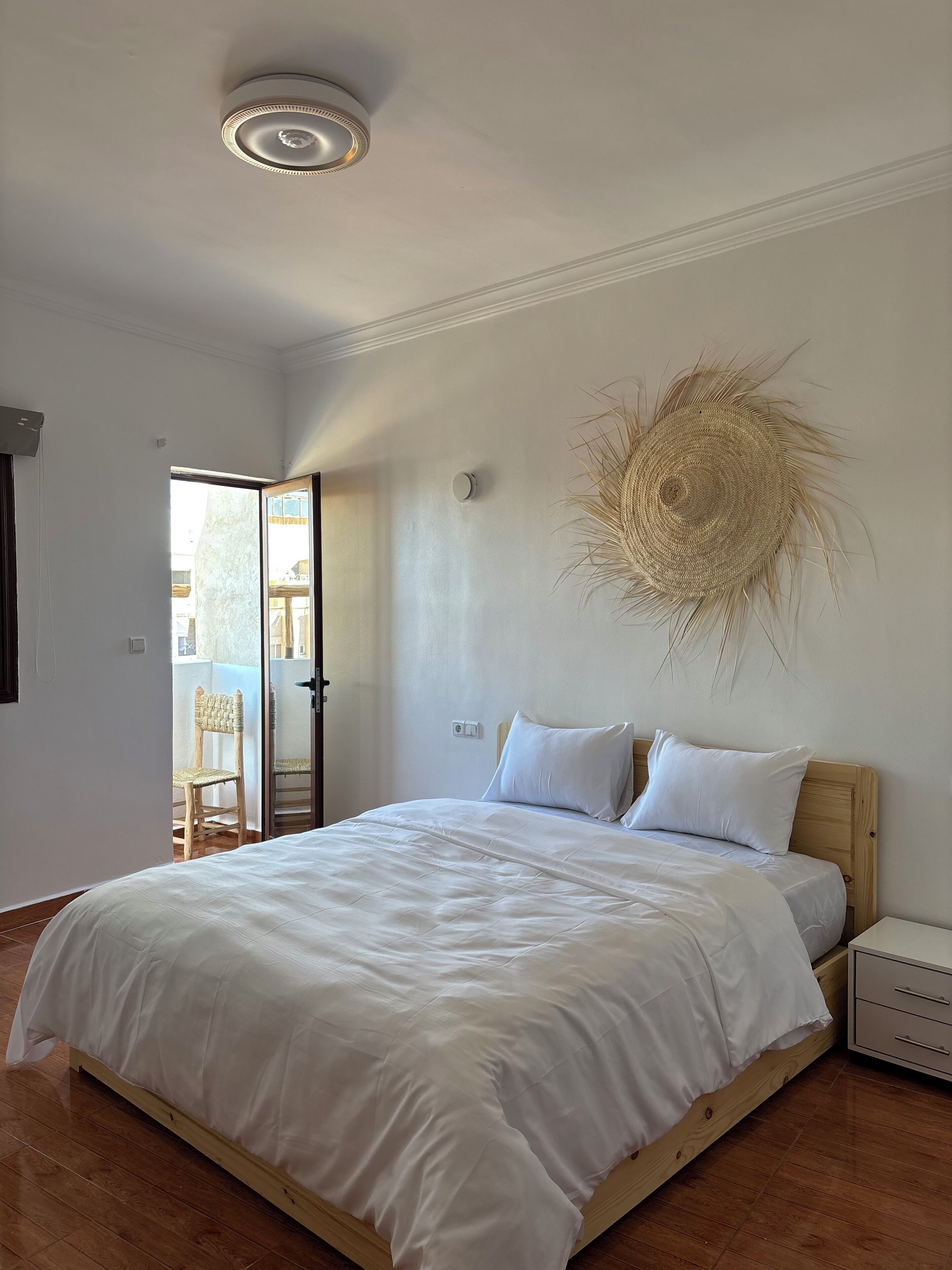 Une chambre à coucher comprenant un lit, une table de chevet, un luminaire fixé au mur et une porte donnant sur un espace extérieur.