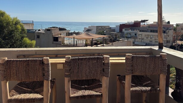 A terrace with wicker chairs, a string of lights, and a view of the sea and buildings. - Tifawave surf stay tamraght (Tamraght)