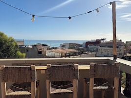Una terraza con sillas de mimbre, luces colgantes y vistas al mar y edificios.