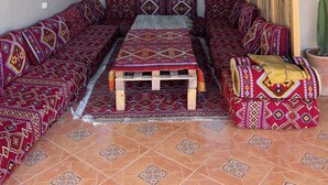 A cozy room with a long sofa, a small table, and a hanging light fixture. - Tifawave surf stay tamraght (Tamraght)