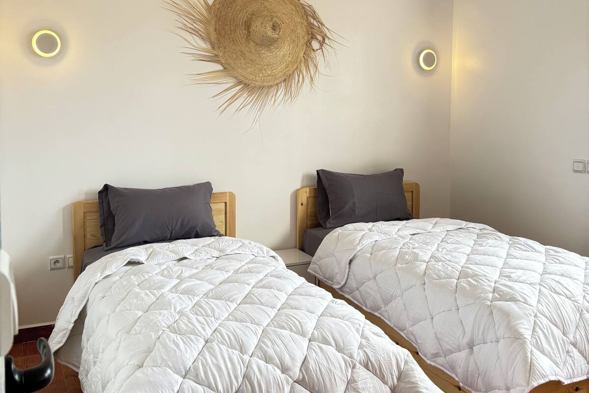 Dos camas con colchas blancas, cabeceros de madera y un adorno en la pared.