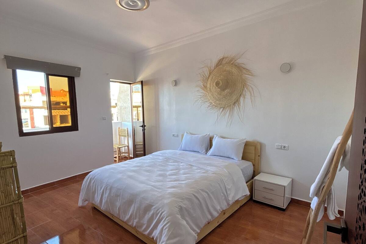 Un dormitorio con una cama grande, suelo de madera, una ventana y una puerta.