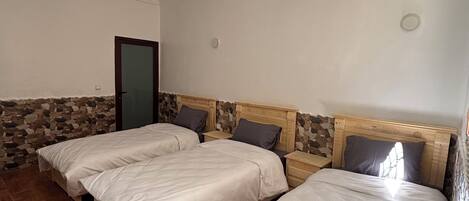 Una habitación con dos camas, una pared de piedra, cabecero de madera, una puerta y una lámpara en el techo.