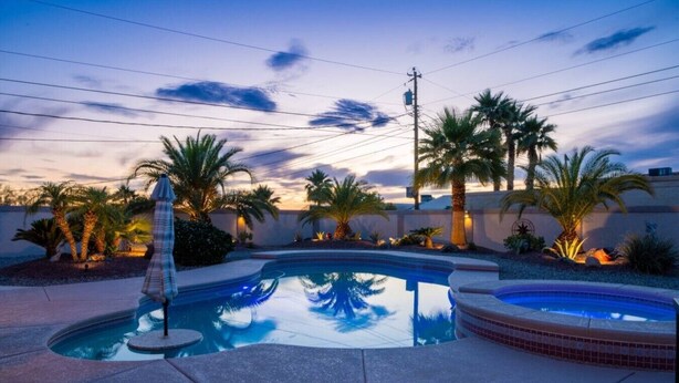 Une piscine avec un jacuzzi, entourée de palmiers et illuminée par le ciel au coucher du soleil.