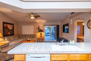 Une cuisine moderne dotée d’un îlot central, un coin repas avec un canapé et une table, et un salon avec un divan et un tableau.