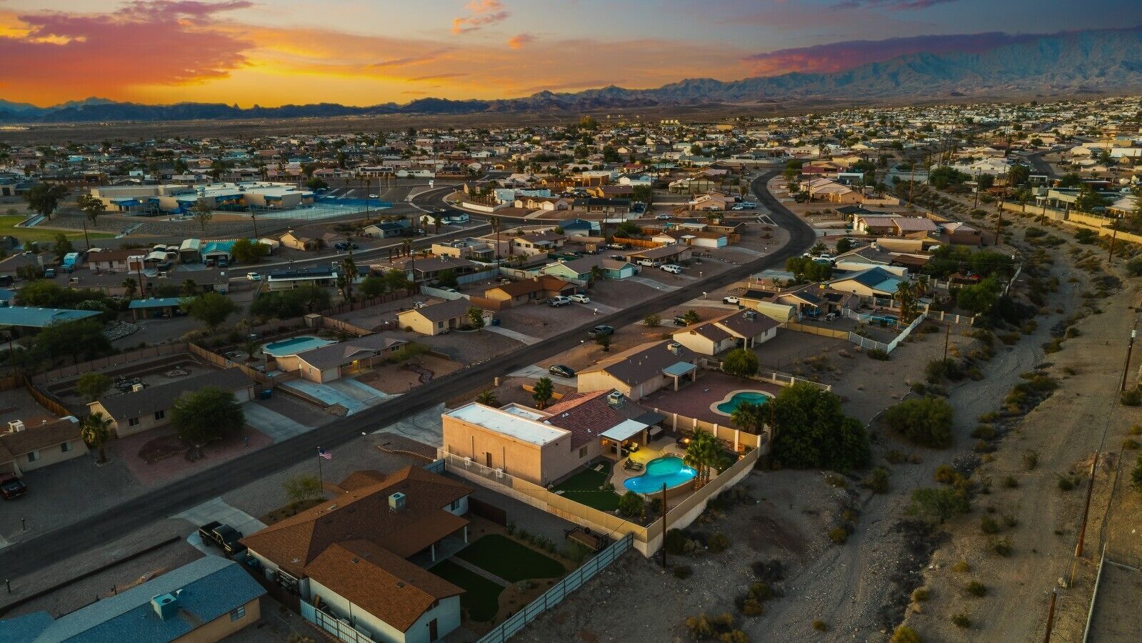 An aerial view of a residential area with houses, roads, and a mountain range in the background.