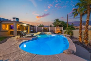 Ein Pool mit Liegestühlen, eine überdachte Terrasse und Blick auf den Sonnenuntergang.