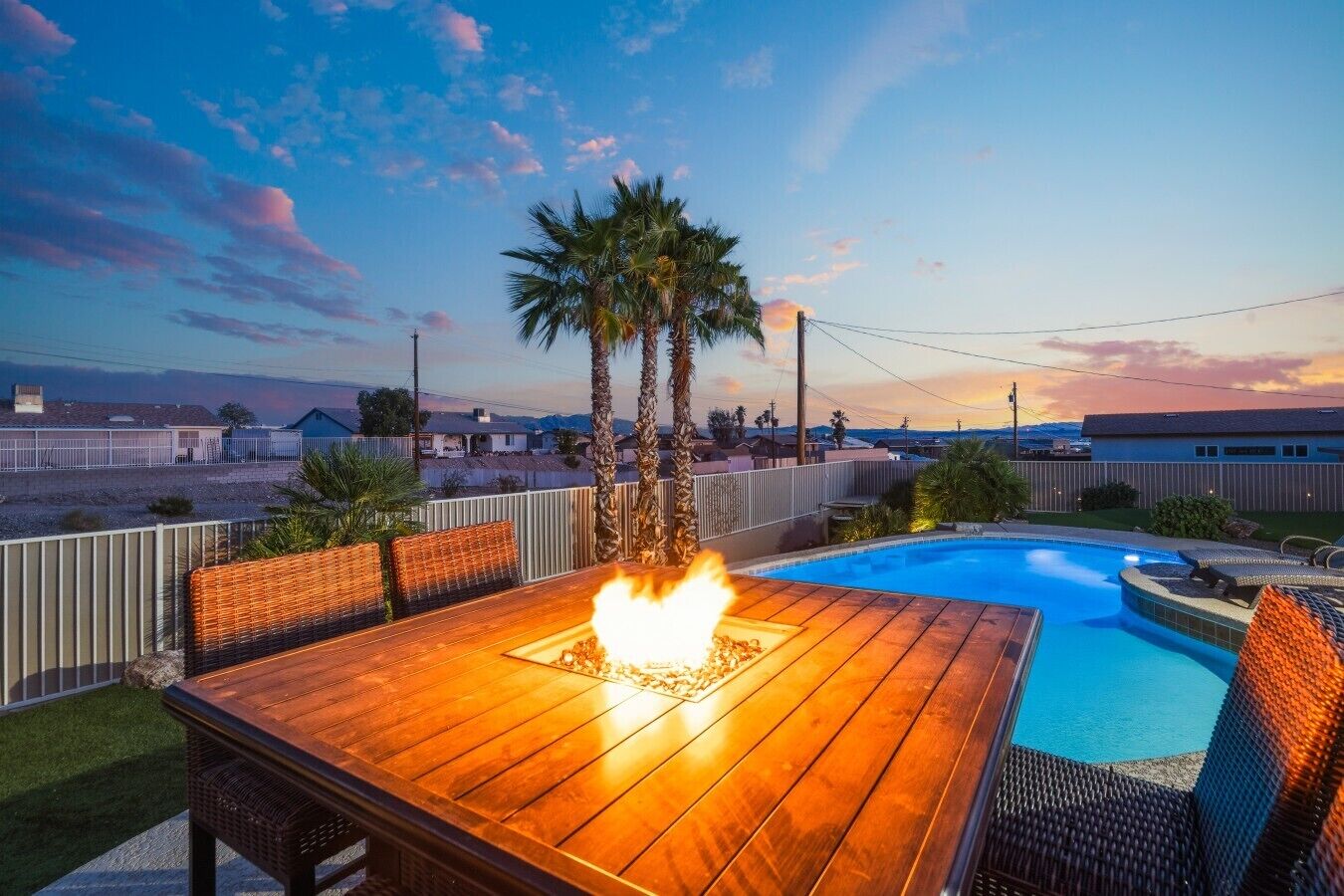 Une terrasse en bois agrémentée d’un foyer extérieur, d’une piscine et de palmiers.