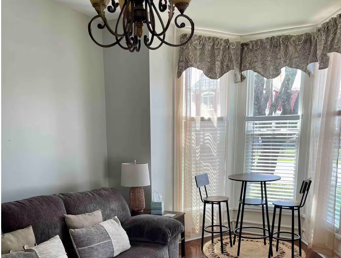 A living room with a sofa, a table with two chairs, a lamp, and a decorative ceiling light.