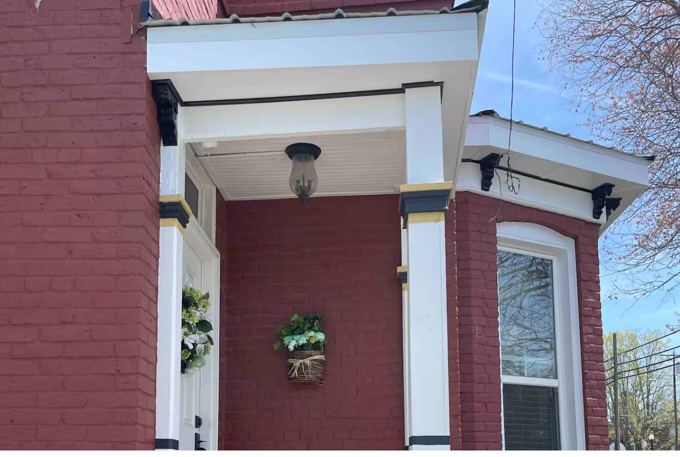 A red brick house with a white porch, a hanging flower basket, and a clear sky.