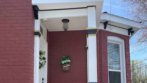 Una casa de ladrillo rojo con un porche blanco, una cesta de flores colgante y un cielo despejado.