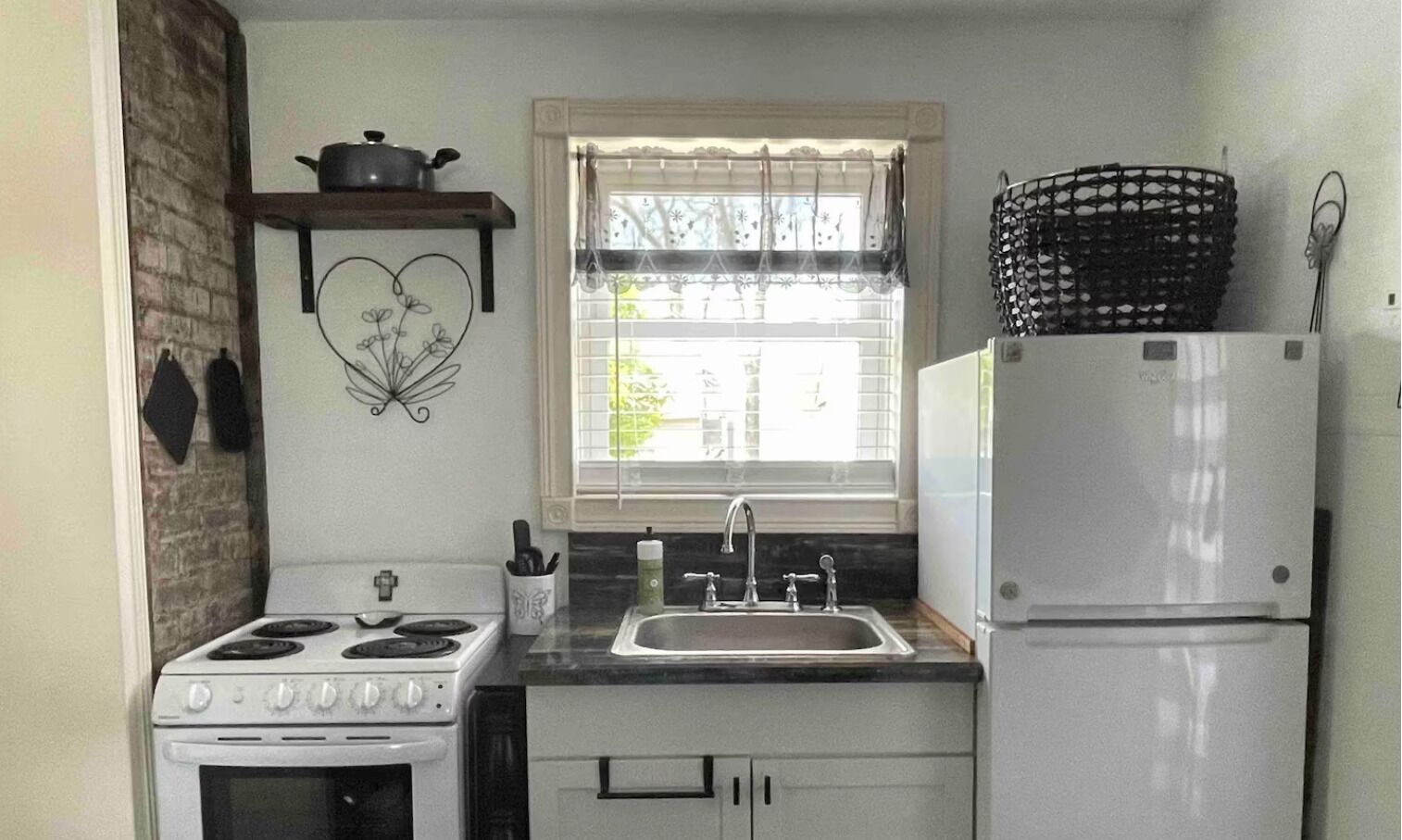 A kitchen with a stove, sink, refrigerator, and a window with blinds.