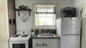 Una cocina con estufa, lavamanos, refrigerador y una ventana con persianas.