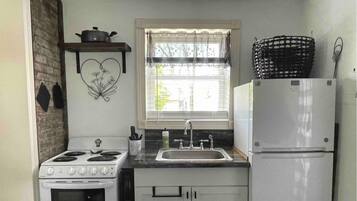 A kitchen with a stove, sink, refrigerator, and a window with blinds.