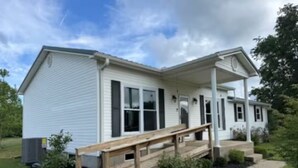 A single-story building with a porch, a small garden area, and a wooden deck. - 3-bedroom farmhouse just minutes from Barkley Lake perfect for relaxing getaways (Marion)
