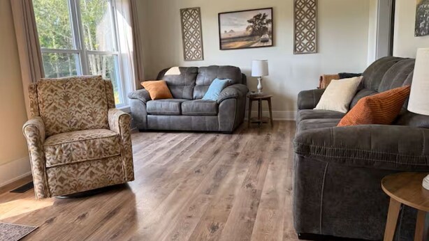 A living room with a patterned armchair, two grey sofas, a wooden floor, and a window with curtains. - 3-bedroom farmhouse just minutes from Barkley Lake perfect for relaxing getaways (Marion)