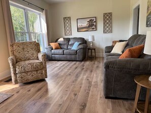 A living room with a patterned armchair, two grey sofas, a wooden floor, and a window with curtains. - 3-bedroom farmhouse just minutes from Barkley Lake perfect for relaxing getaways (Marion)