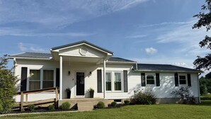 A single-story house with a front porch, a garage, and a well-maintained lawn. - 3-bedroom farmhouse just minutes from Barkley Lake perfect for relaxing getaways (Marion)