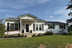 A single-story house with a front porch, a garage, and a well-maintained lawn. - 3-bedroom farmhouse just minutes from Barkley Lake perfect for relaxing getaways (Marion)