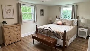 A bedroom with a wooden floor, a bed with a metal frame, a wooden bench, a dresser, and two windows with curtains. - 3-bedroom farmhouse just minutes from Barkley Lake perfect for relaxing getaways (Marion)