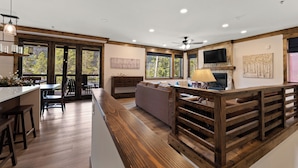 Un intérieur moderne comprenant une cuisine, un coin repas et un espace de vie, avec des poutres en bois, de grandes fenêtres et une cheminée.