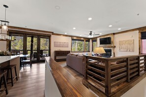 A modern interior with a kitchen, dining area, and living space, featuring wooden beams, large windows, and a fireplace.