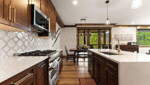Une cuisine avec des meubles de rangement en bois, une cuisinière, un four à micro-ondes et un grand îlot central doté d’un évier.