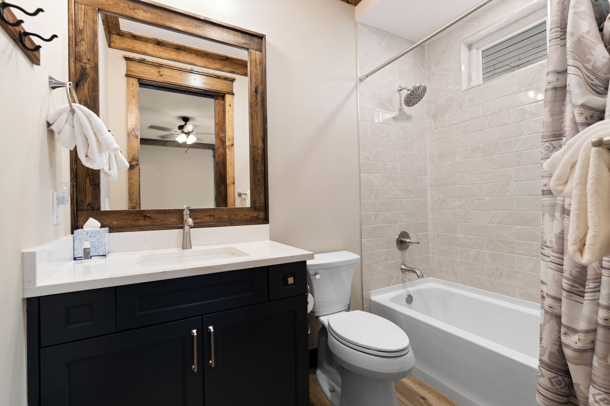 A bathroom with a white sink, dark cabinets, a white toilet, a bathtub, and a shower with a white tiled wall.