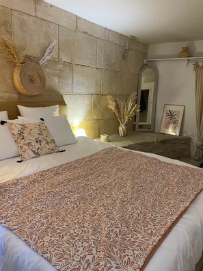 Ein Schlafzimmer mit Steinwand, einem Bett mit gemusterten Textilien, einem gewebten Korb und einer Vase mit Pampasgras.