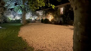 Uma entrada de cascalho conduz a um prédio com uma grande árvore em primeiro plano.