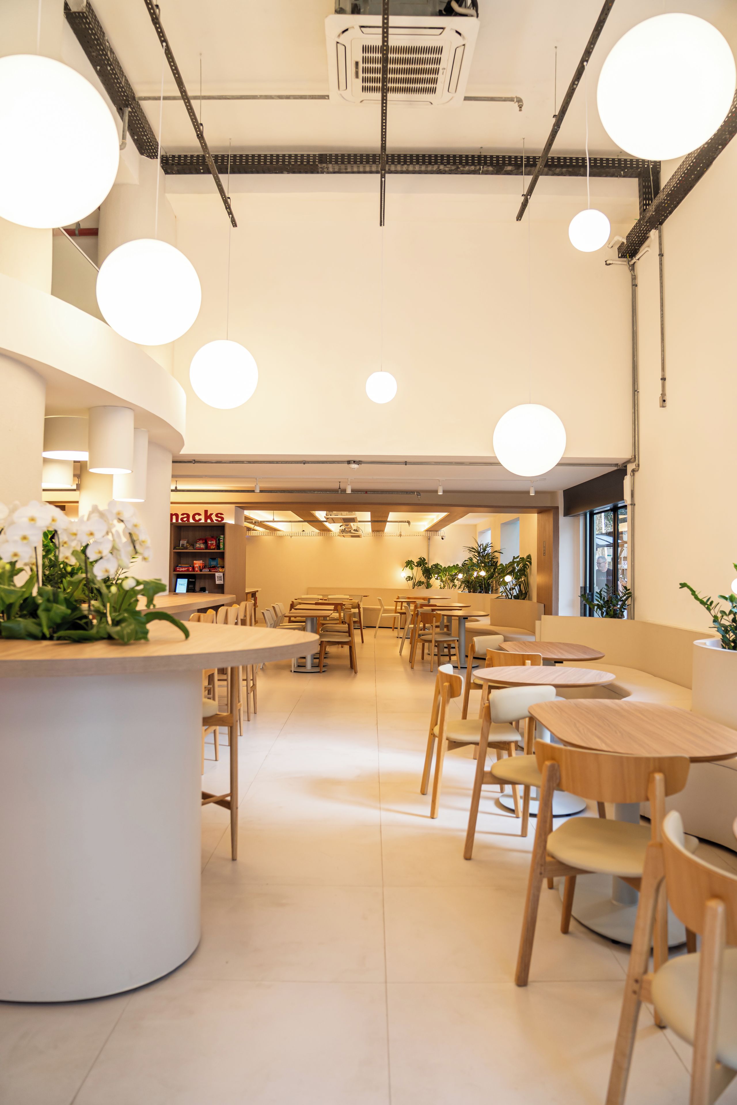 A modern cafe interior with round tables and chairs, a central white counter, and hanging spherical lights.