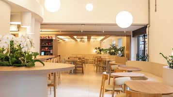 A modern cafe interior with round tables and chairs, a central white counter, and hanging spherical lights.