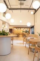 Un interno di un caffè moderno con tavoli e sedie rotonde, un bancone bianco centrale e lampade sferiche a sospensione.