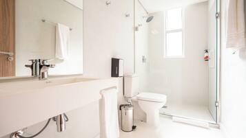 Un baño moderno con cabina de ducha de vidrio, inodoro blanco y lavabo con espejo sobre él.