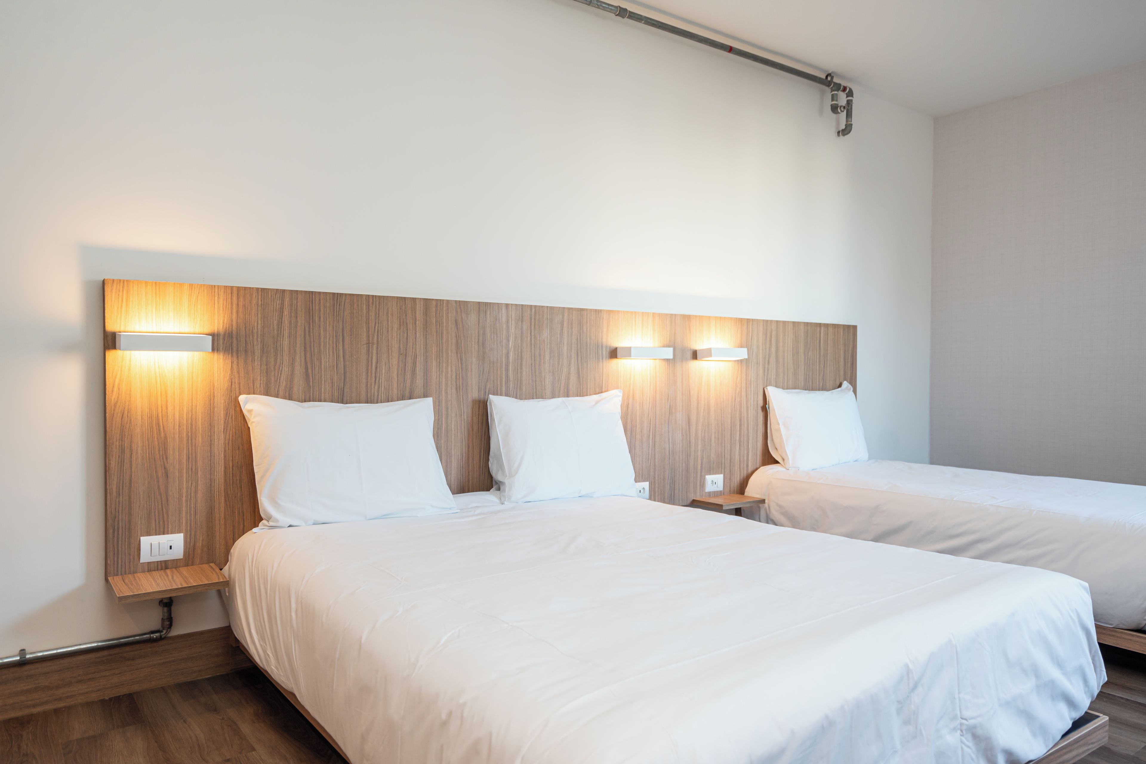 A hotel room with two beds, wooden headboards, and wall-mounted lighting.