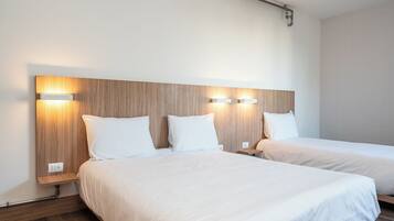A hotel room with two beds, wooden headboards, and wall-mounted lighting.