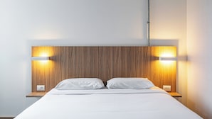 Un lit bien fait, avec du linge de lit blanc, une tête de lit en bois et deux lampes de chevet.