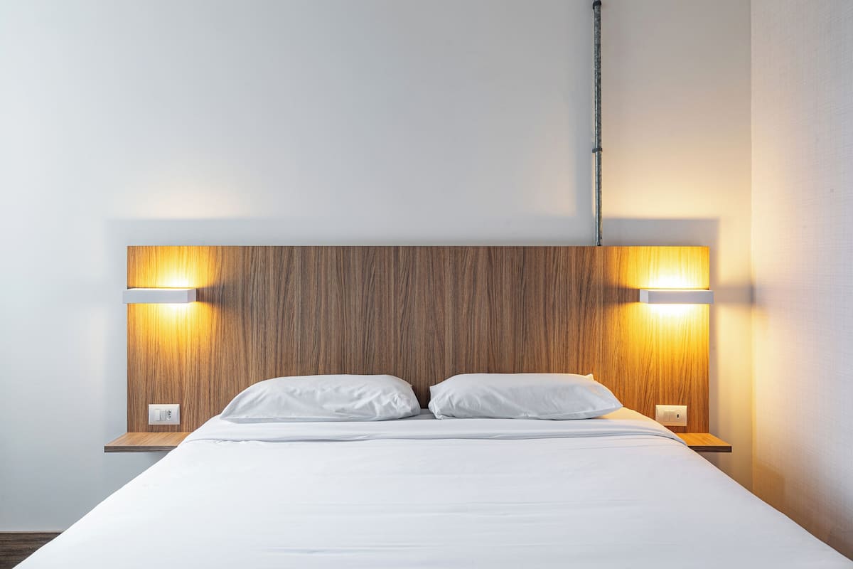 A neatly made bed with white linens, a wooden headboard, and two bedside lamps.