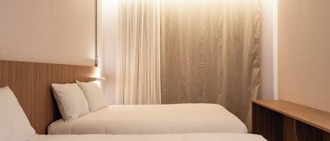 Ein Hotelzimmer mit zwei Betten, einem Holzkopfteil, einem Nachttisch und einem Fenster mit leichtem Vorhang.