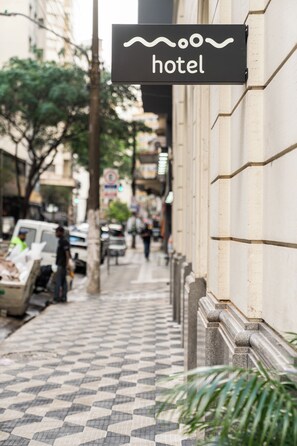 Señal de hotel en un edificio con un pavimento de baldosas y una calle al fondo.