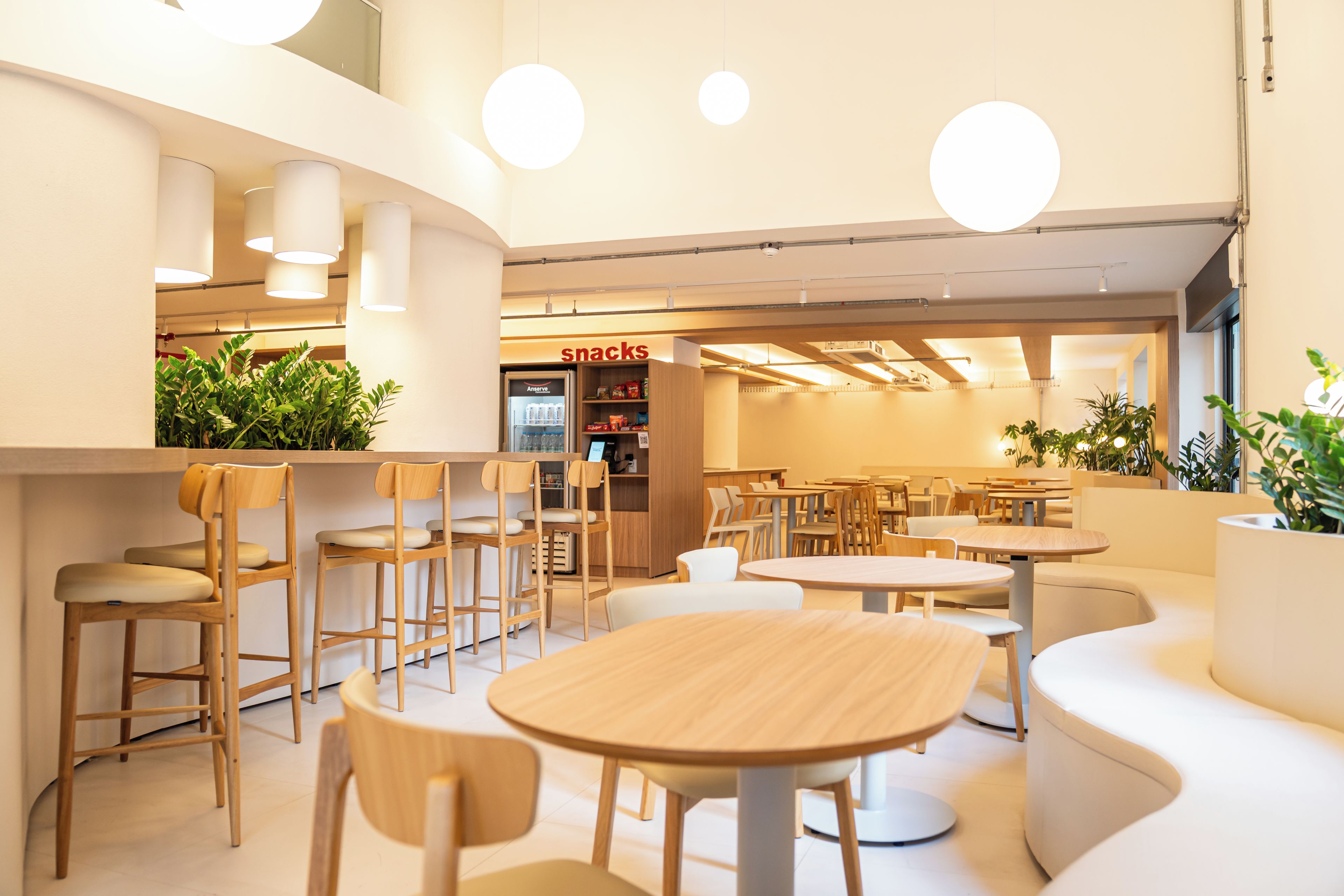 Un interno di un caffè moderno con tavoli rotondi e sedie di legno, un bancone per snack in vista e piante in vaso.