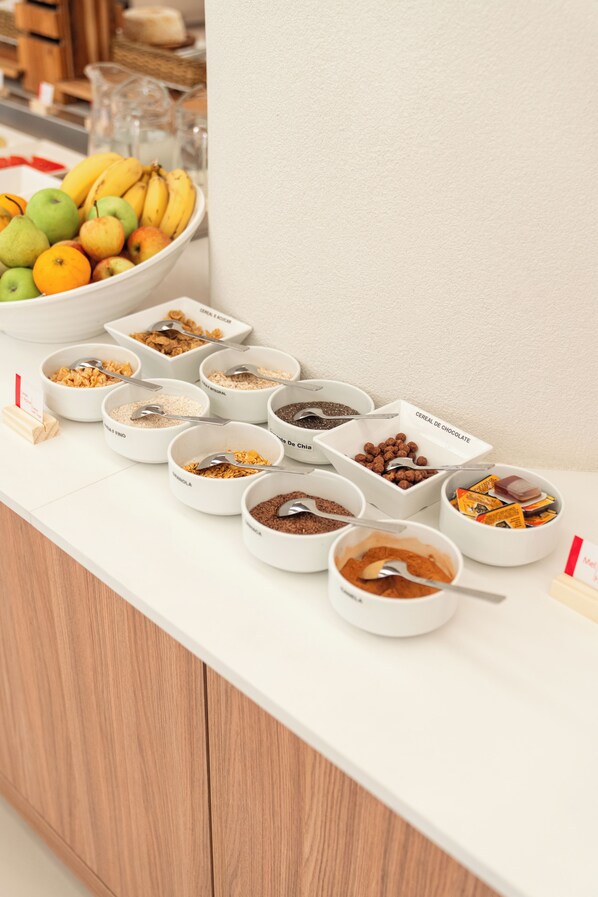 Un bufé de desayuno con distintos cereales y frutas.